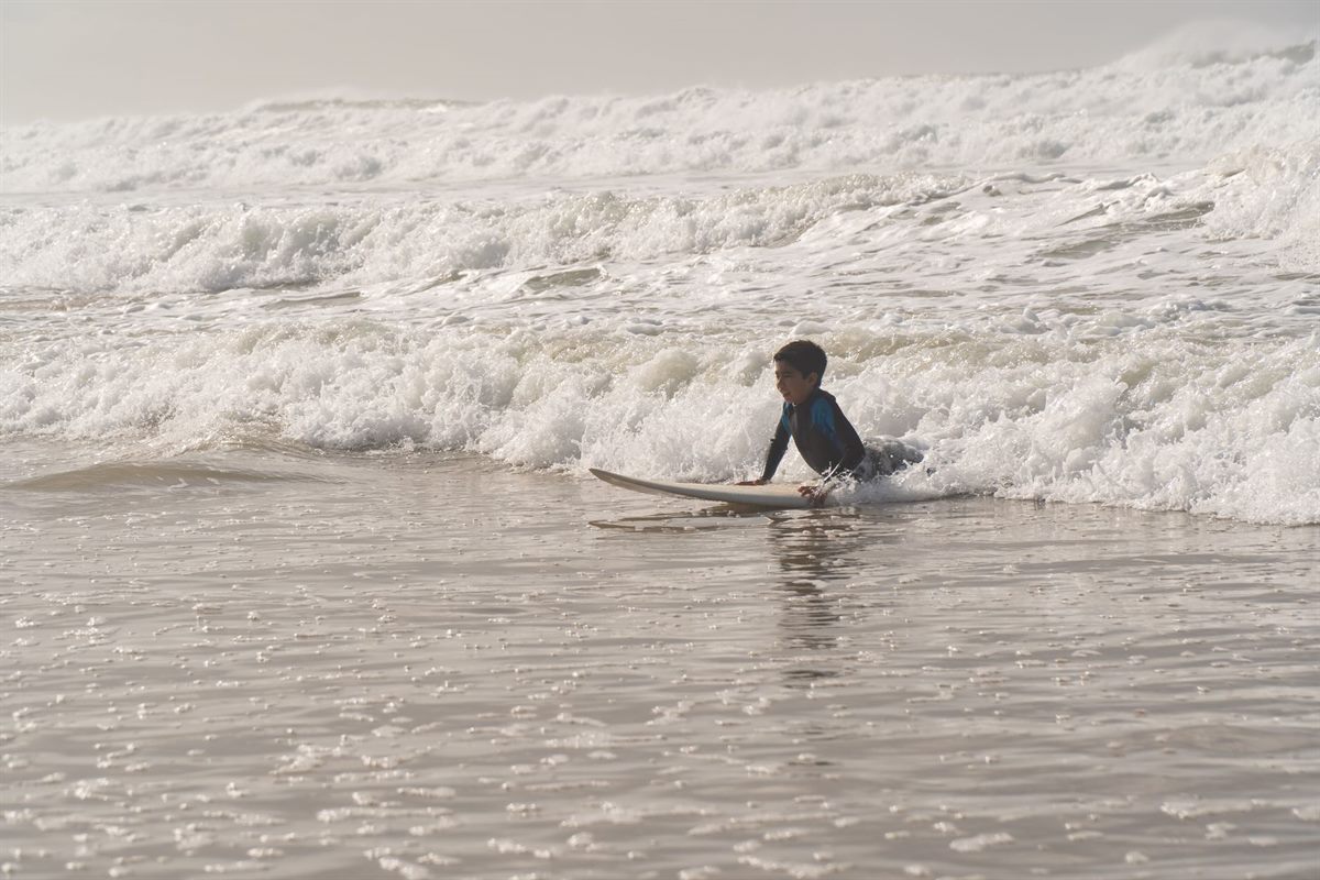 A child learning to surf in gentle whitewater with an instructor in Taghazout